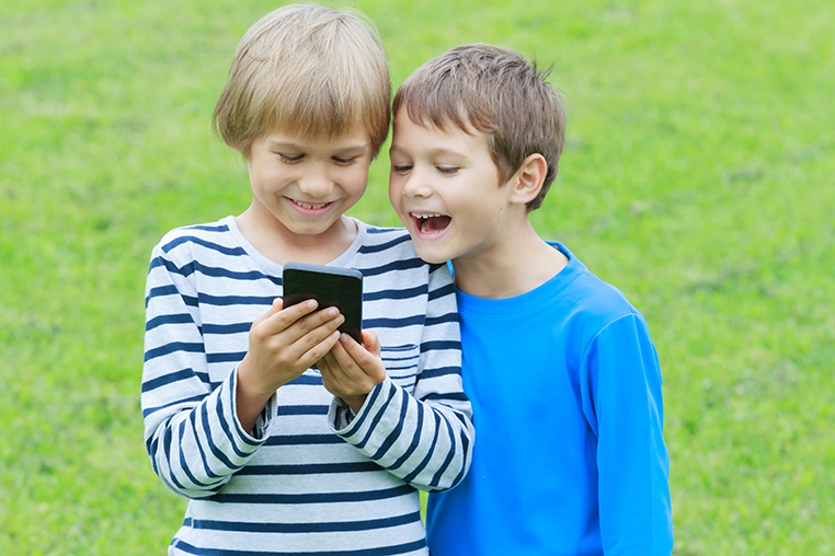 Boys with mobile phone. Children smiling, looking to screen, playing games or using application. Outdoor. Technology education leisure people concept
