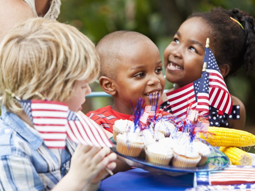 Three kids sharing cupcakes and corn decorated with patriotic streamers