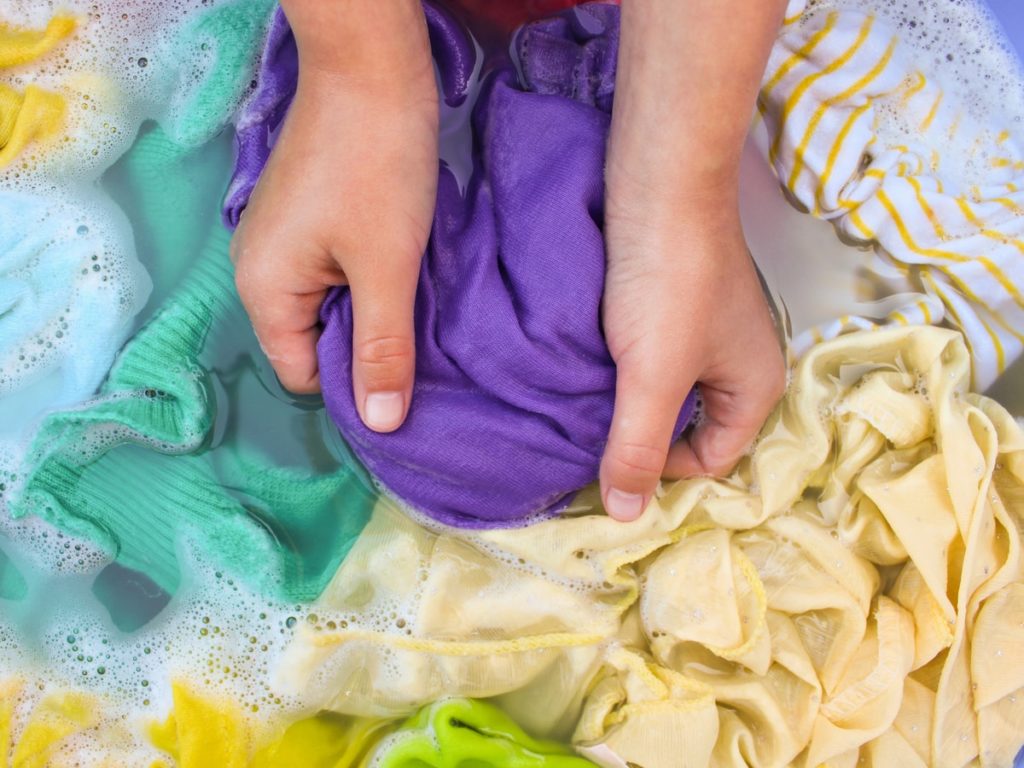 Hands scrubbing colorful clothes in soapy water