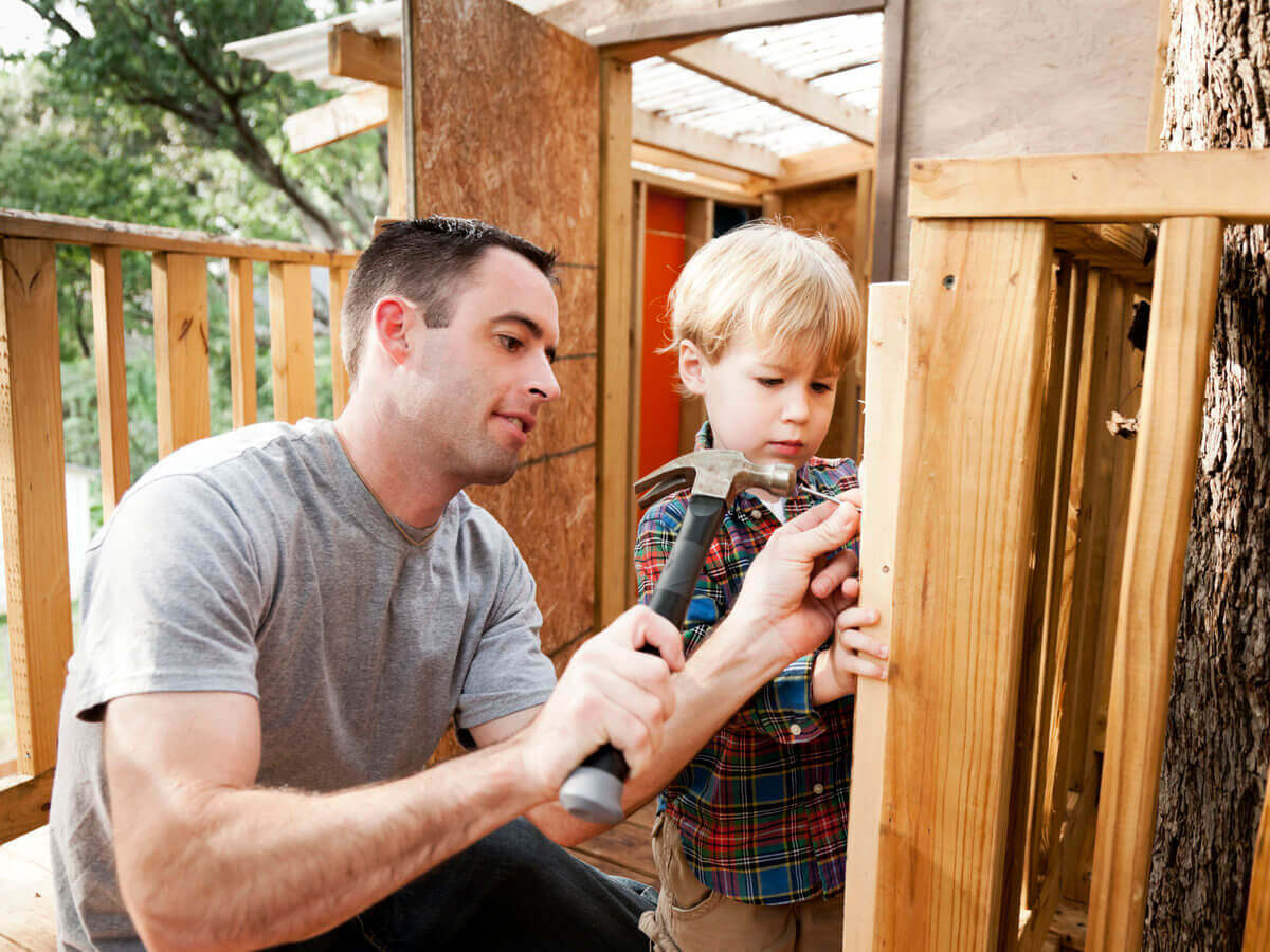 Father and son using hammer and nails to build a wooden kids fort