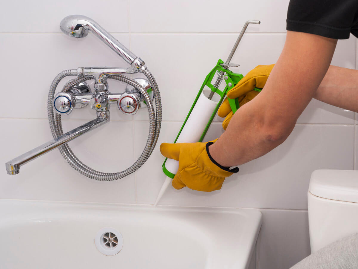 Wearing gloves to re-caulk and re-grout shower bath tub