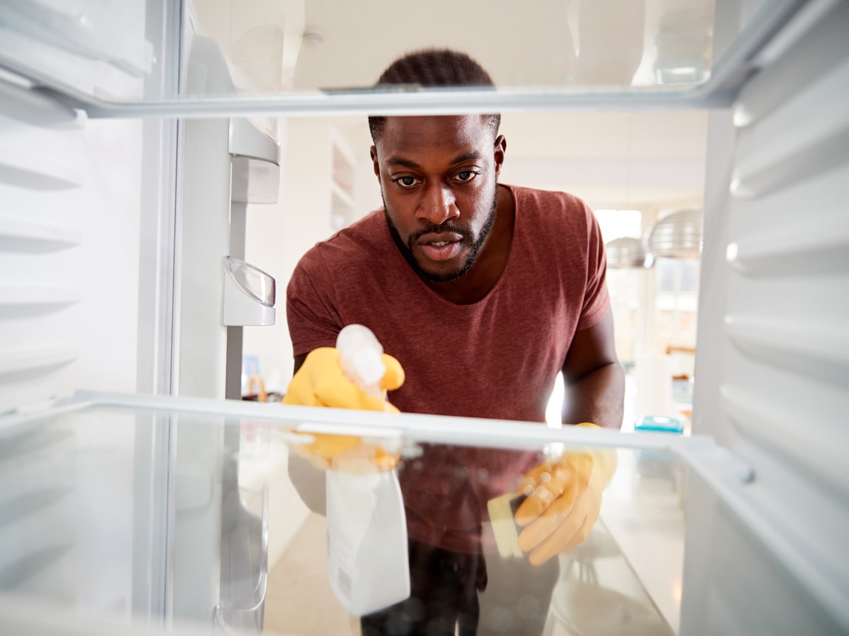 Man spraying cleaner into empty fridge