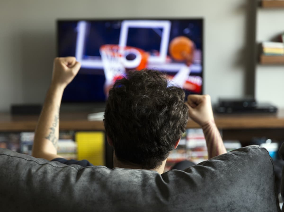 Man sitting on couch excitedly watching a basketball game. 