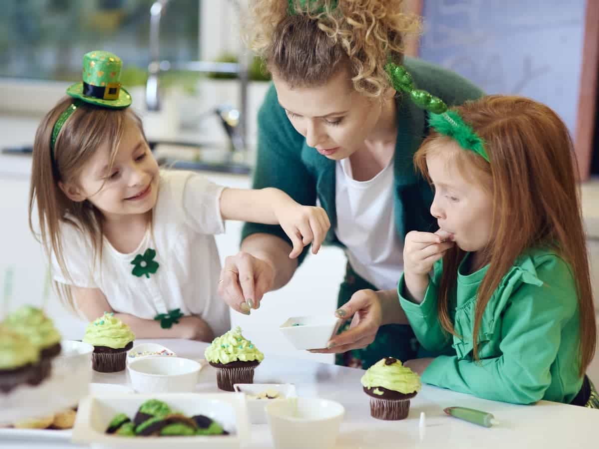 A mother and two young daughters dressed in green and decorating St. Patrick's Day cupcakes
