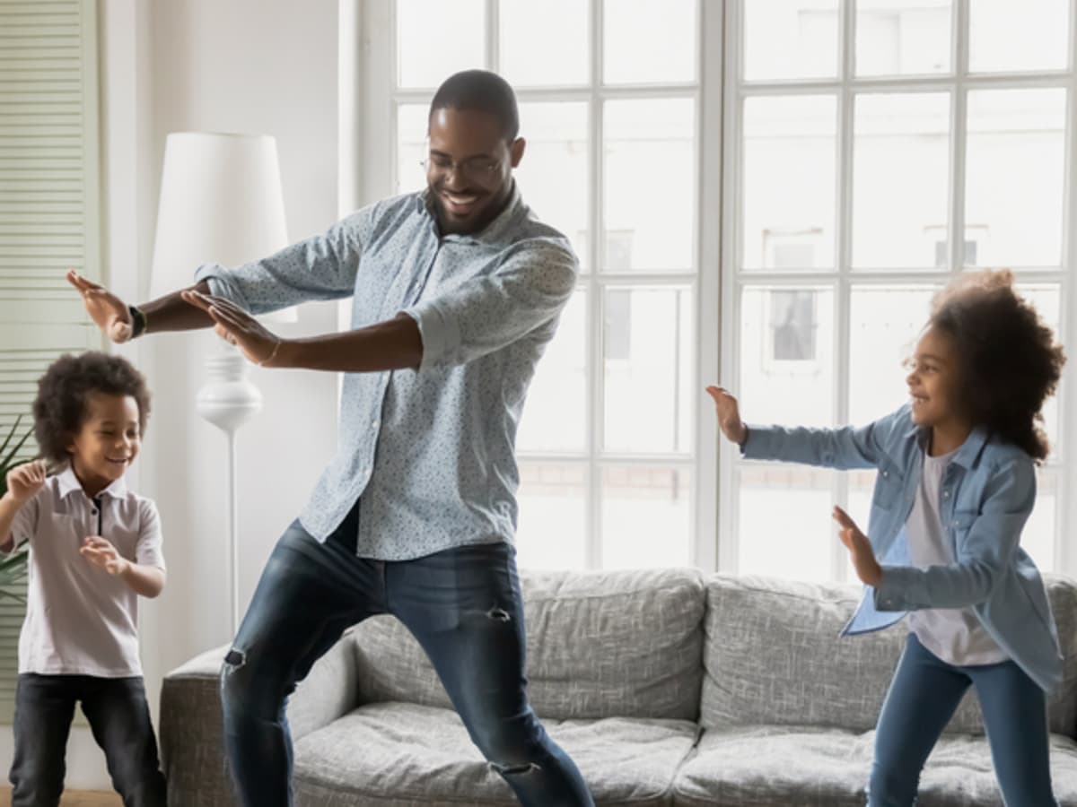 A father and his two children dancing in living room together.