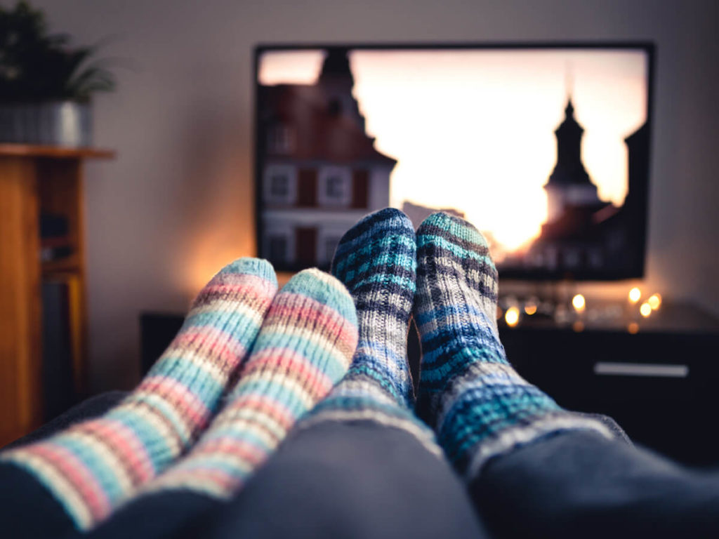 two pairs of feet in fuzzy socks in front of a tv with twinkle lights around it