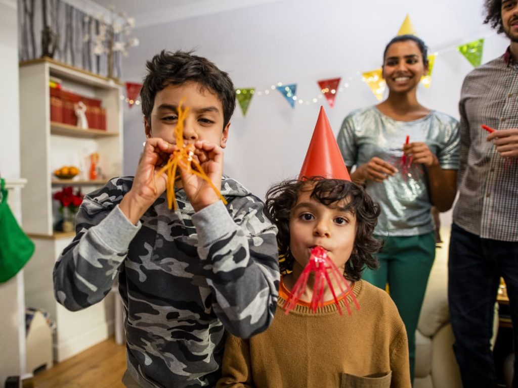 Family of four celebrating New Years with streamers, hats, and other supplies.