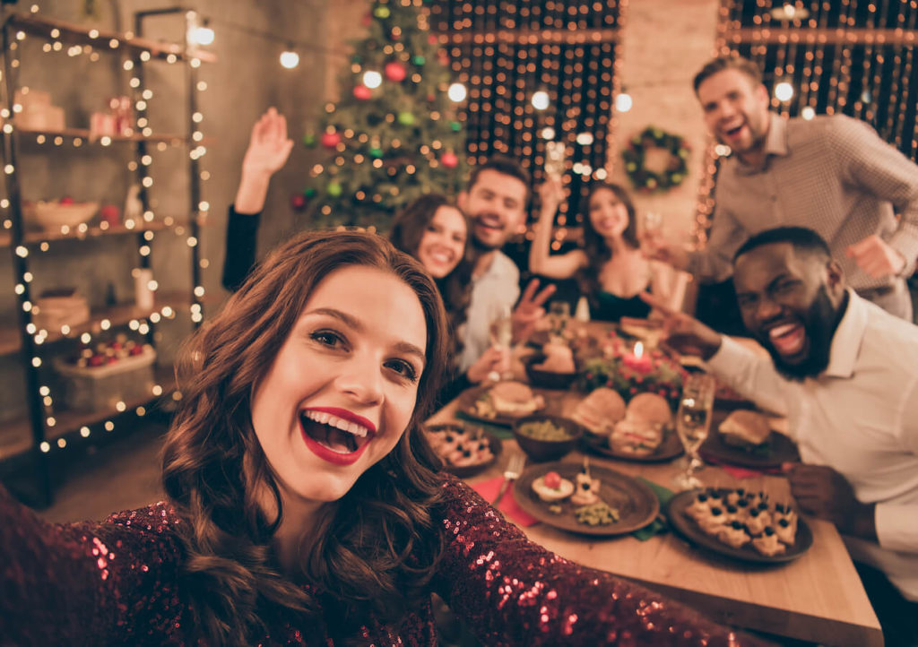 Young adult friends and family gather around a dinner table to celebrate the holiday season with food, drinks, and decor.