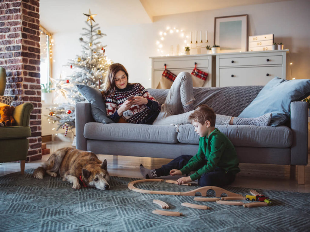 Mother and young son are spending time in their living room as he plays with a train set and she relaxes.