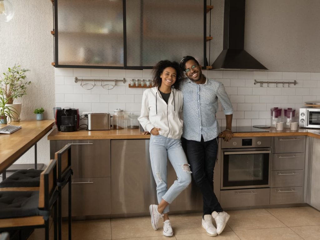 Couple leaning against counter in kitchen while smiling at camera.