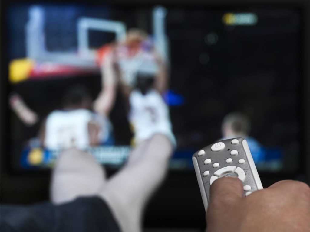 Image of man watching basketball game while holding remote