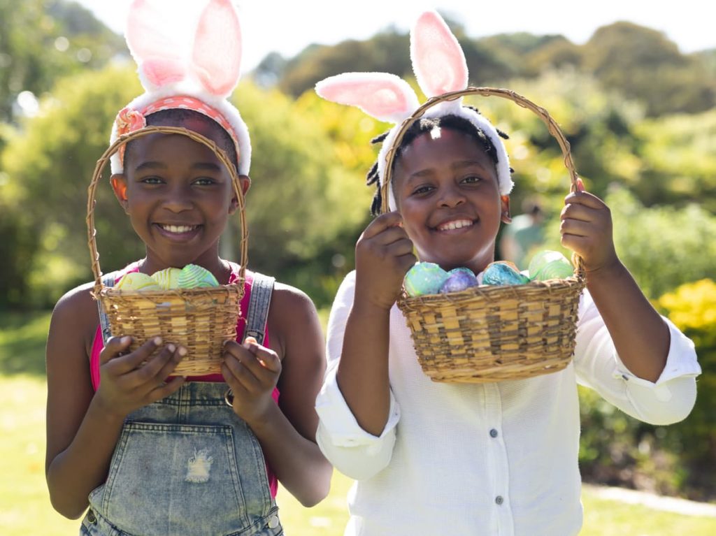 Two children with bunny ears smiling for camera while holding easter baskets