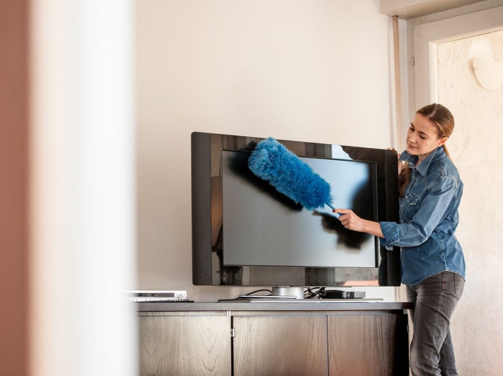 Woman using blue duster to clean TV screen