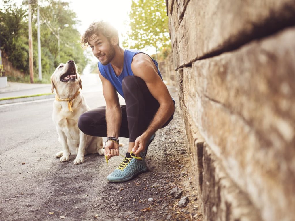 Man in athletic wear tying his shoes next to a brick wall with dog