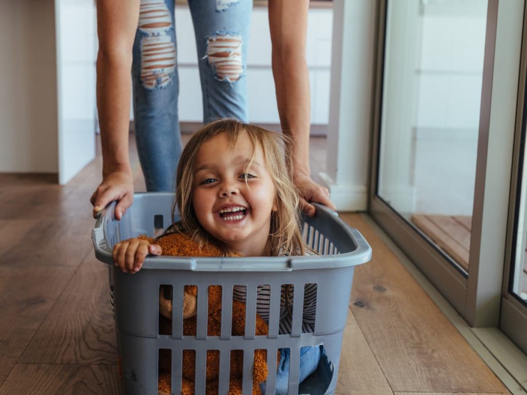 Mom pushing young smiling daughter in laundry basket