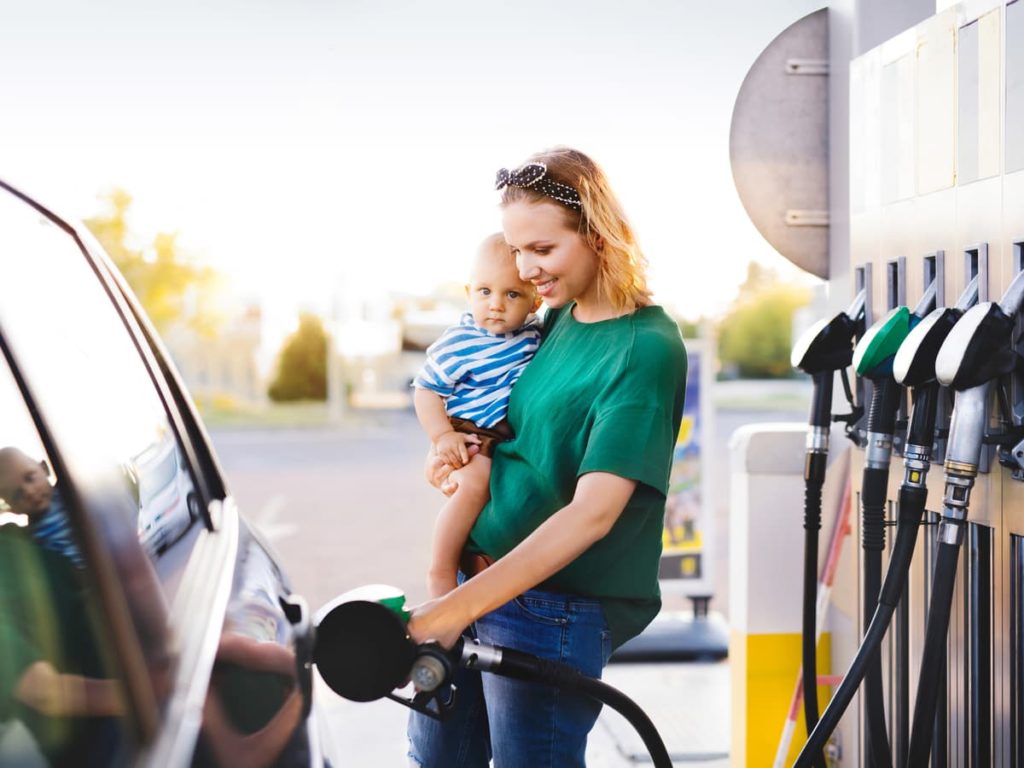 Woman holding infant while pumping gas at the fuel pump