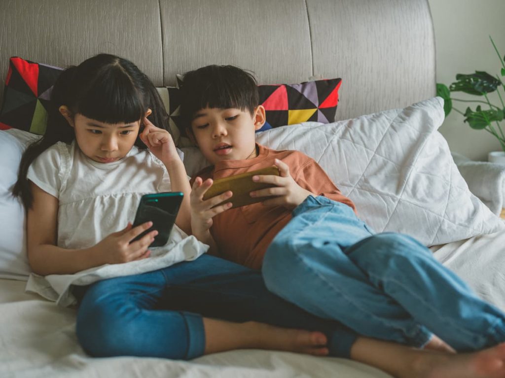 Two children sitting in bed on their smartphones.