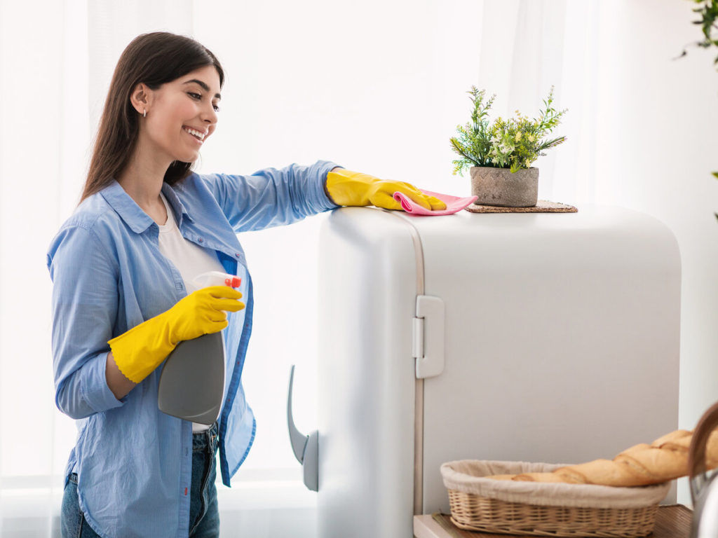 Smiling woman wiping down the top of her refrigerator