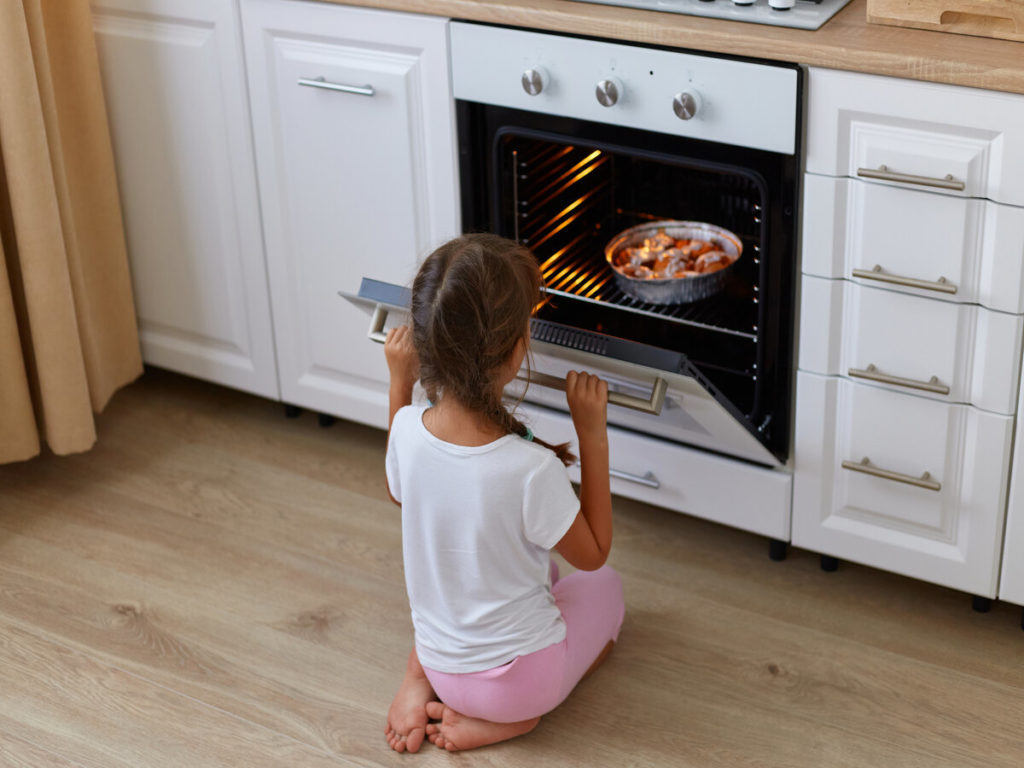 Little girl sitting on floor near oven looking at sweet rolls