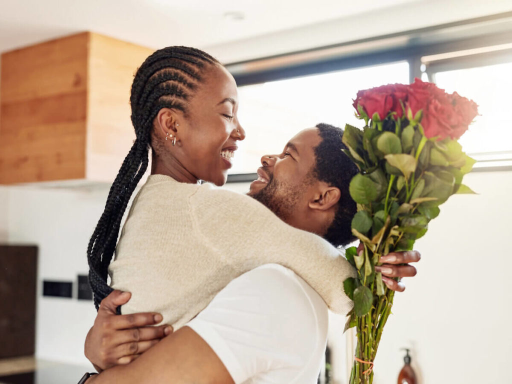 Man hugs woman who is holding a bouquet of red roses.