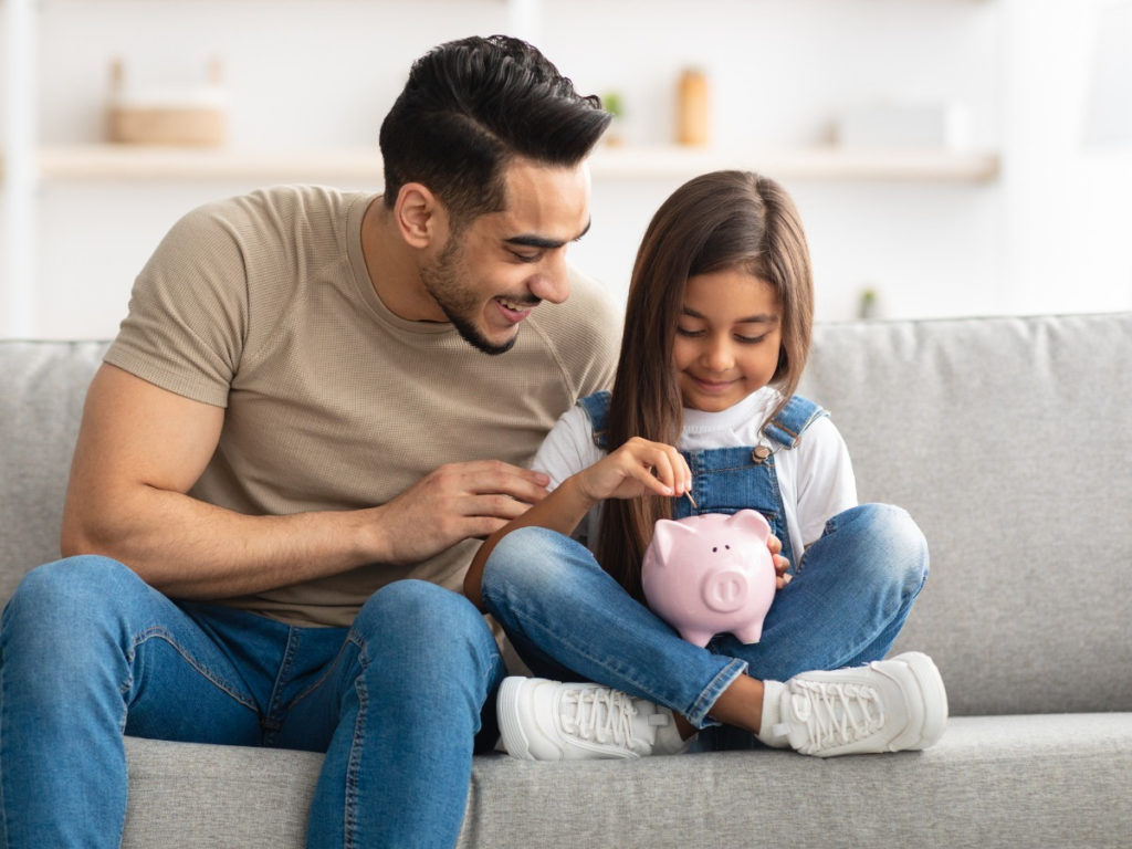 Young girl and her dad putting money into a piggy bank
