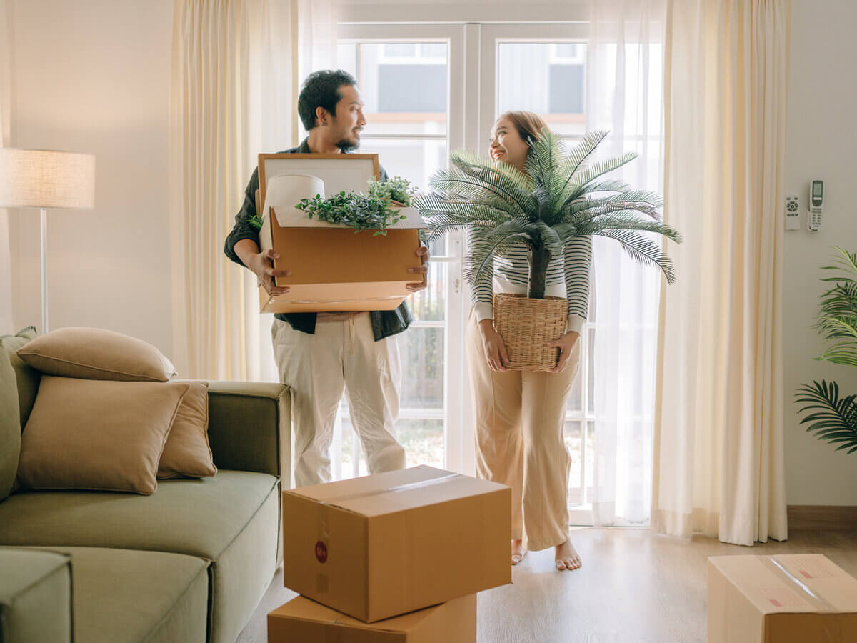 Smiling couple packing boxes in bright living room.