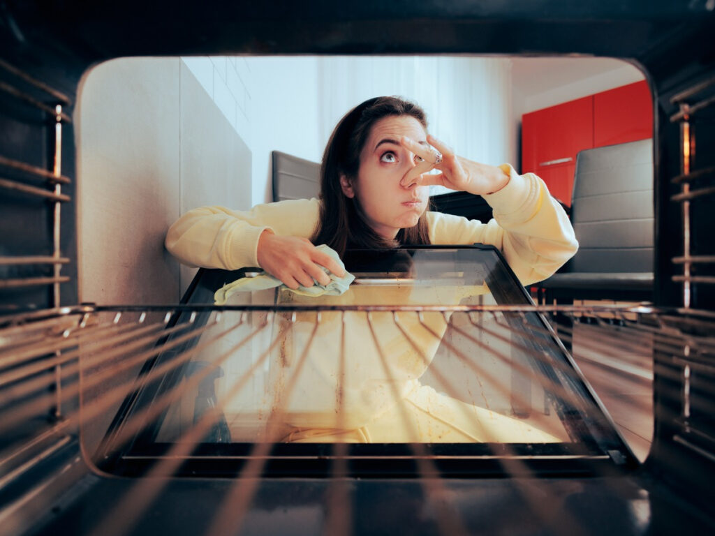Woman looking inside oven while holding nose due to strange smell