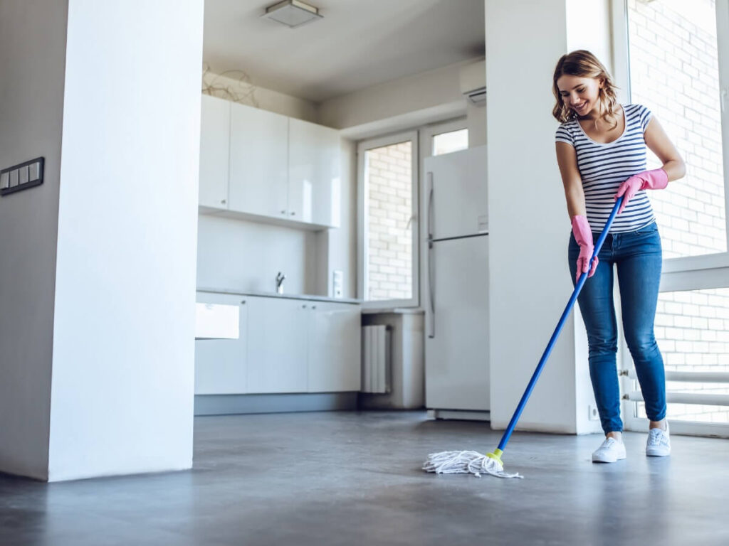 Smiling woman with pink gloves mopping floor in empty apartment