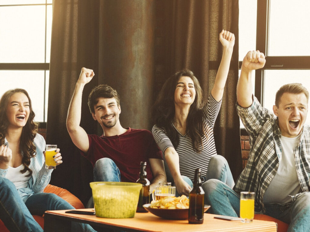 Group of friends cheering on sofa while watching TV