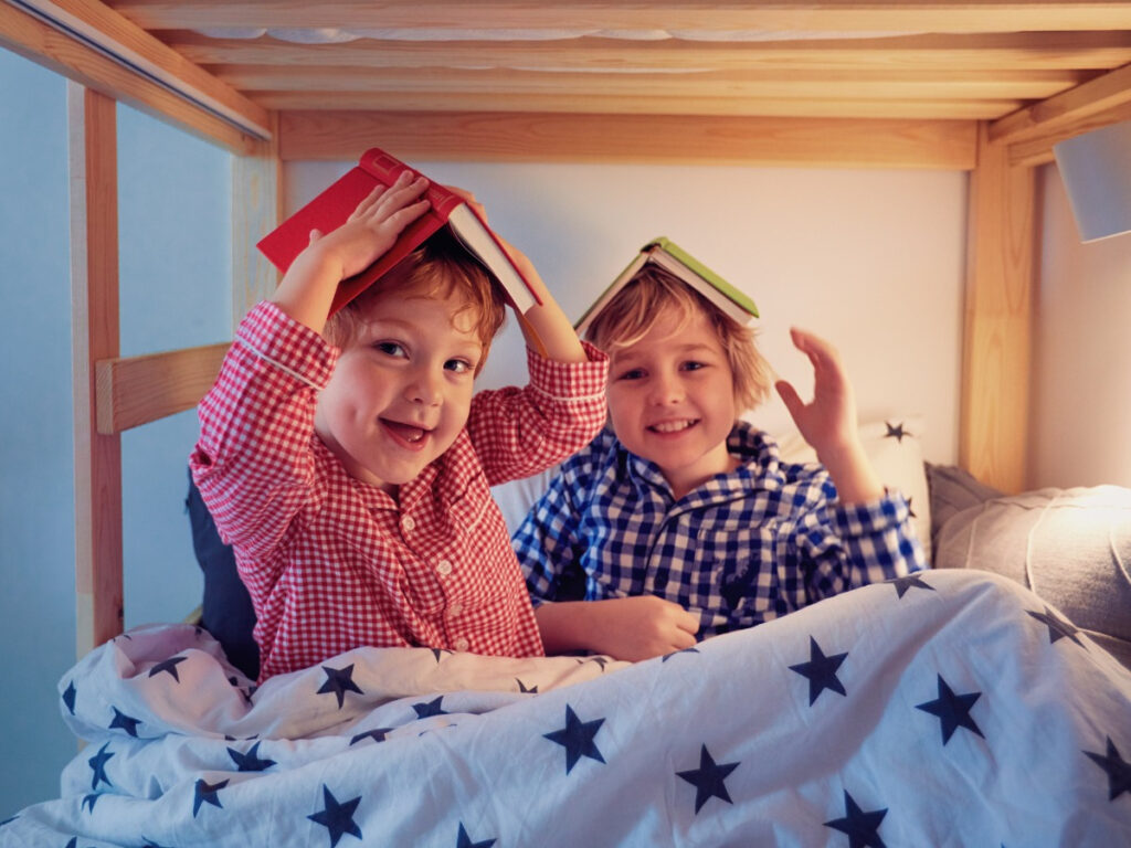 Two smiling young boys in bed with books on their head
