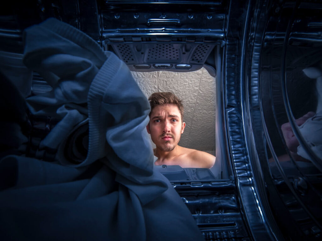 Viewpoint from inside dryer with concerned man looking inside.