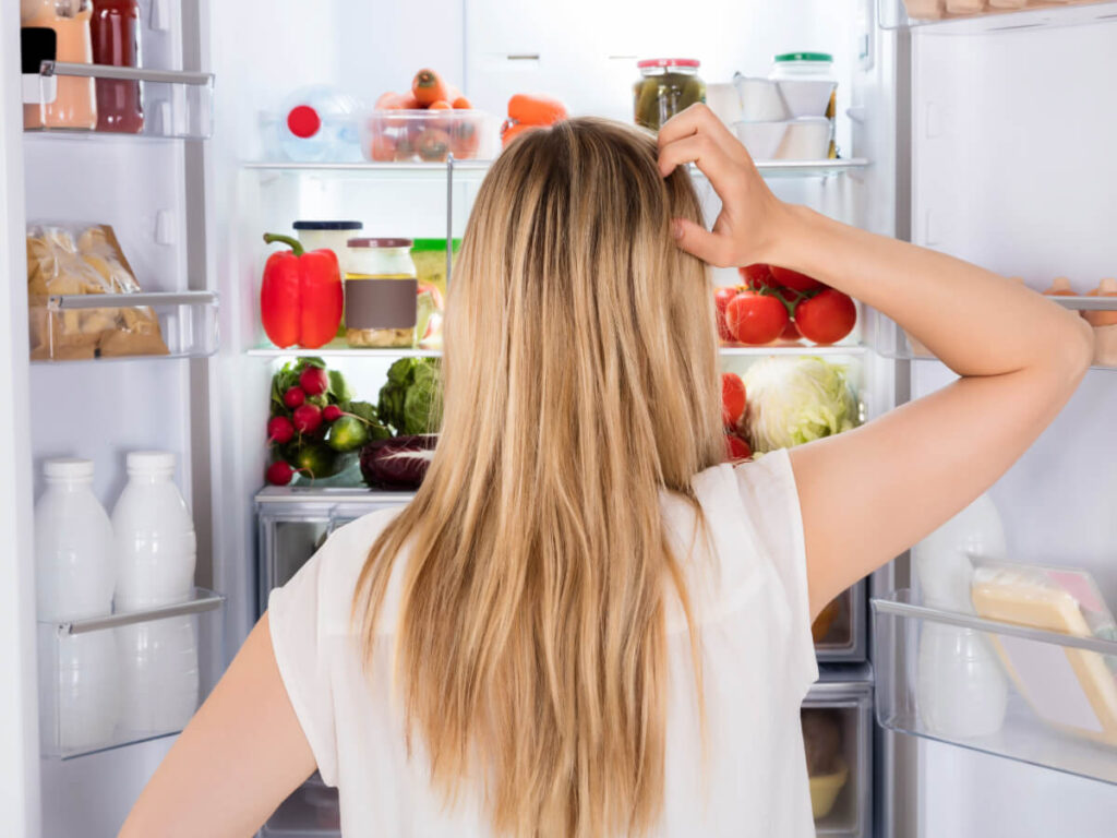Back of woman looking into fridge with perplexed demeanor