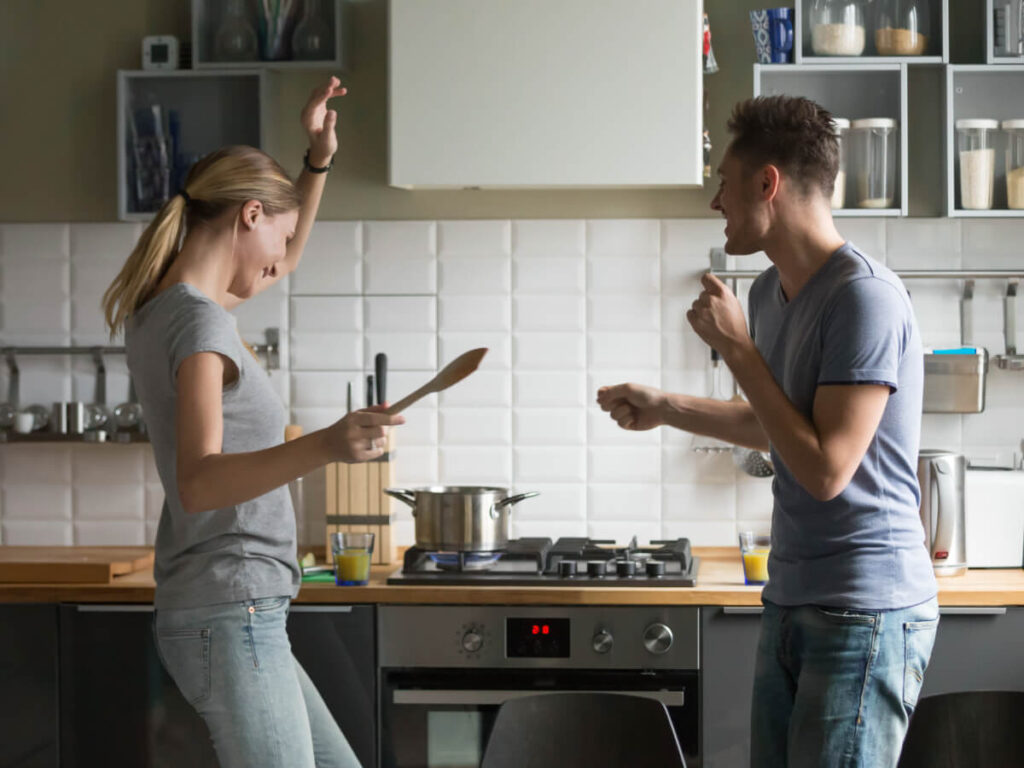 Man and woman in kitchen dancing and smiling as they boil food in a pot on the range