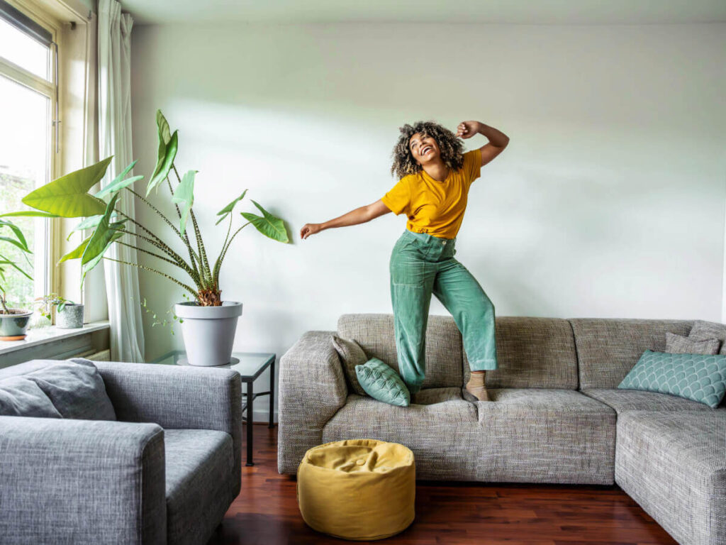 A happy woman standing on her sofa, dancing.