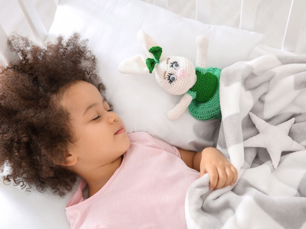 Cute toddler girl sleeping peacefully next to bunny toy in big kid bed