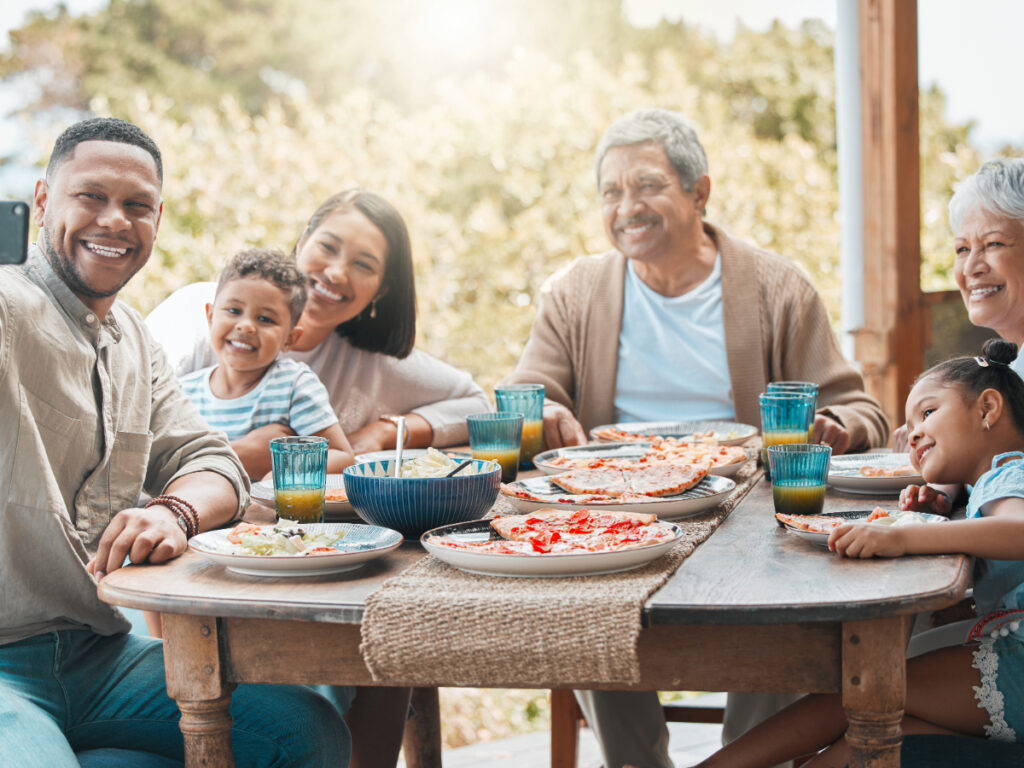 Happy multigenerational family smiling and taking photo at outside dinner table while seated