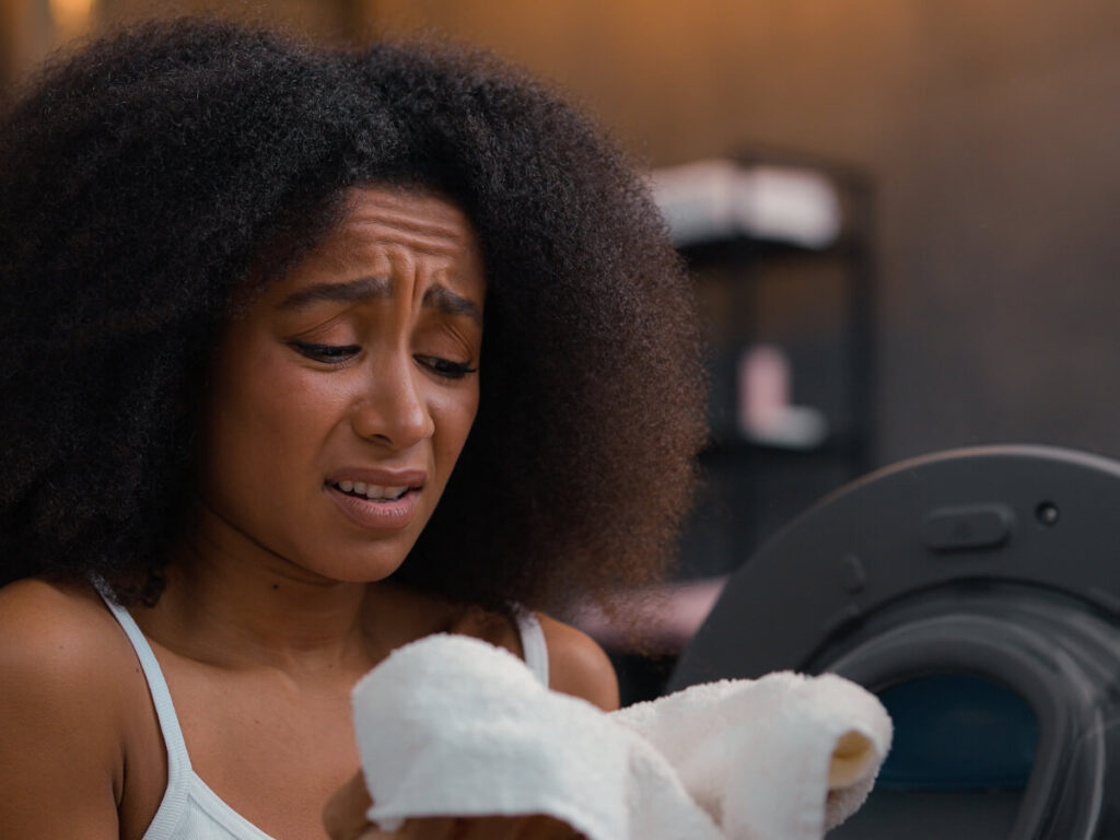 Frowning woman with white towel in hand while sitting next to a dryer