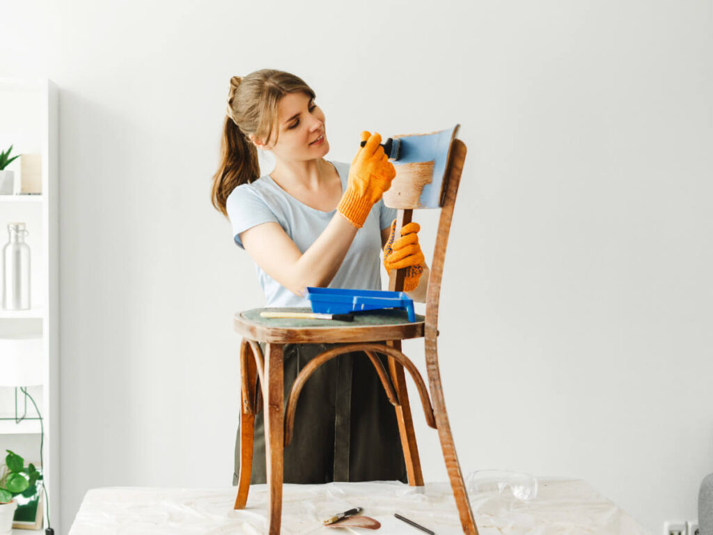 Smiling woman painting a wooden chair in her home