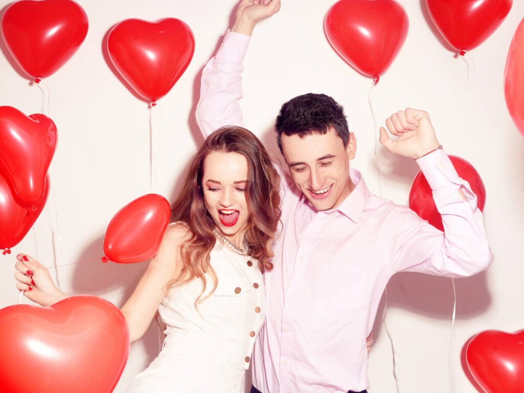 Couple dancing against white backdrop with live red heart balloons