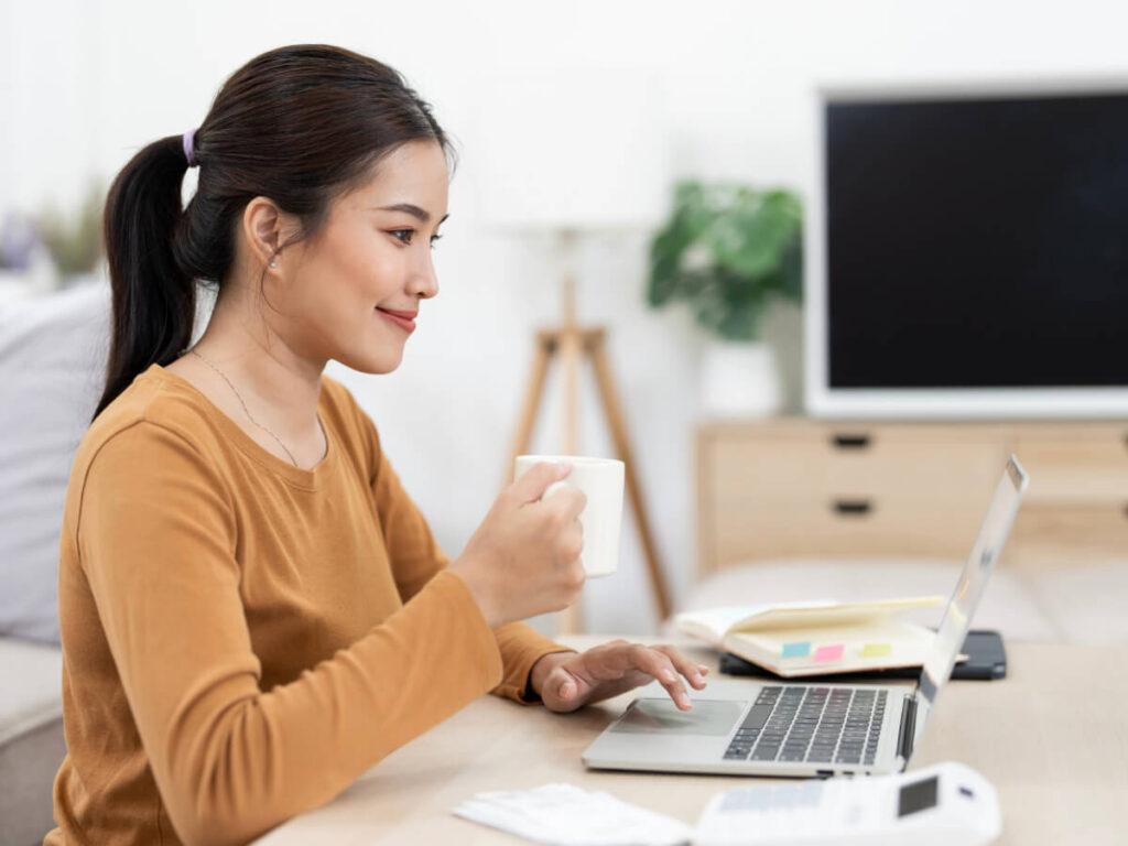 Smiling woman sitting at home desk with cup of coffee in hand