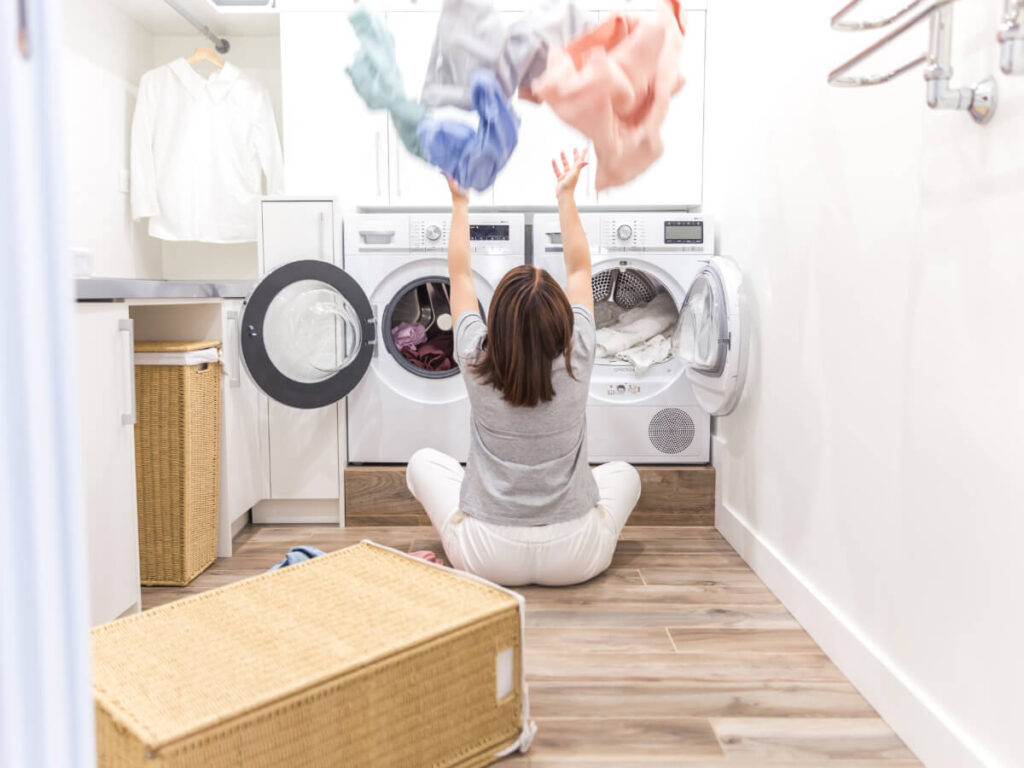 Woman sitting in front of washer and dryer happily tossing clothing in the air