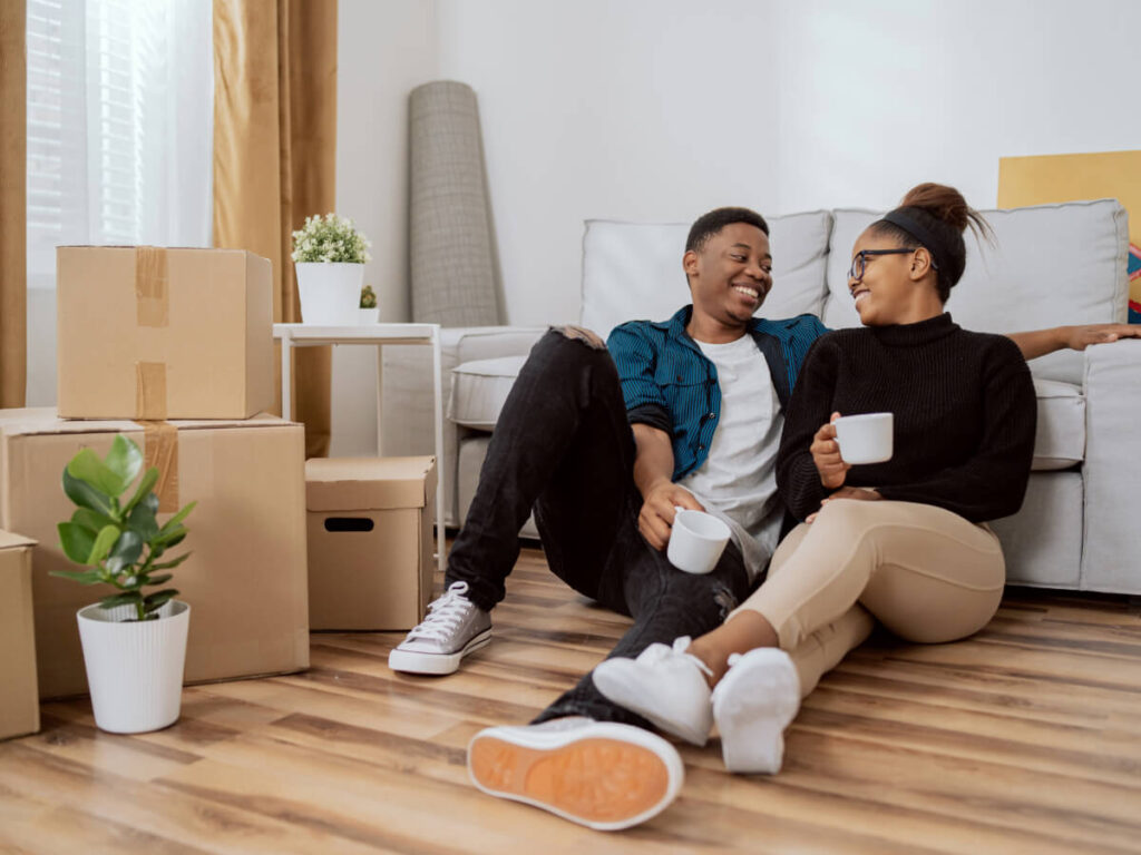 Smiling couple looking at each other while sitting on new living room floor surrounded by moving boxes