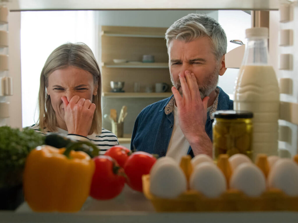 Couple Holding Their Noses While Looking in Fridge filled with groceries