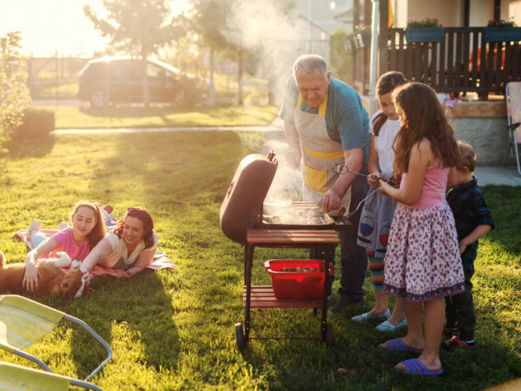 Multi-generational family grilling on BBQ pit in backyard on a beautiful, sunny day.