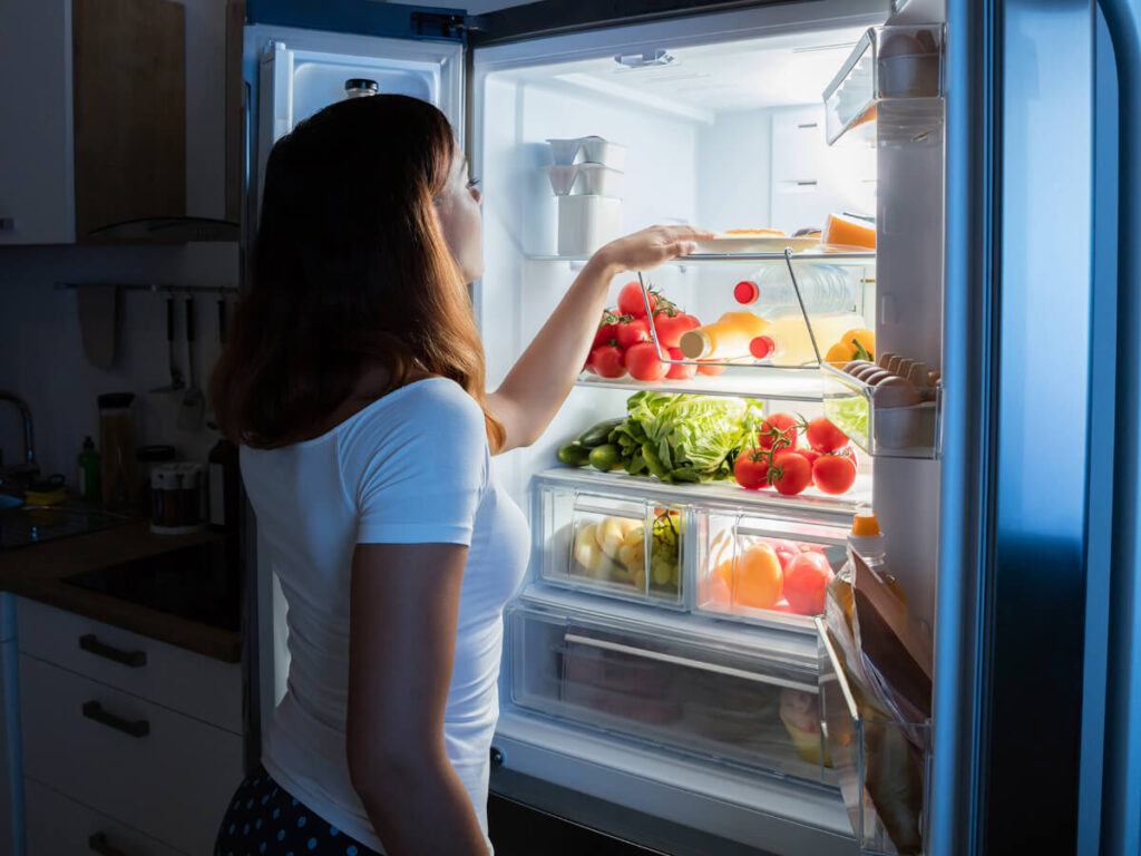 Concerned woman looking into fridge with fresh fruits and veggies