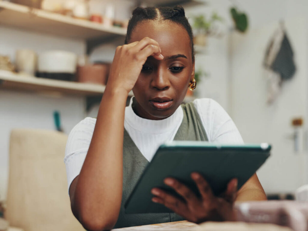 Woman sitting at desk on tablet looking pensive or frustrated