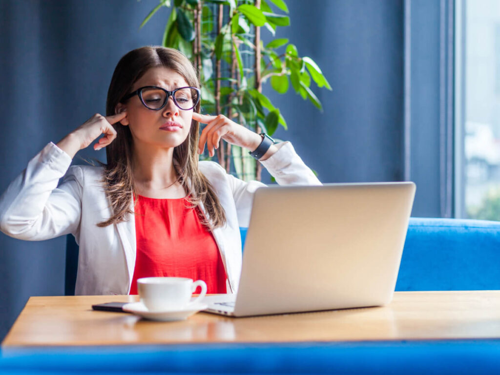 Woman Plugging Her Ears While Sitting in Front of a Laptop at her desk