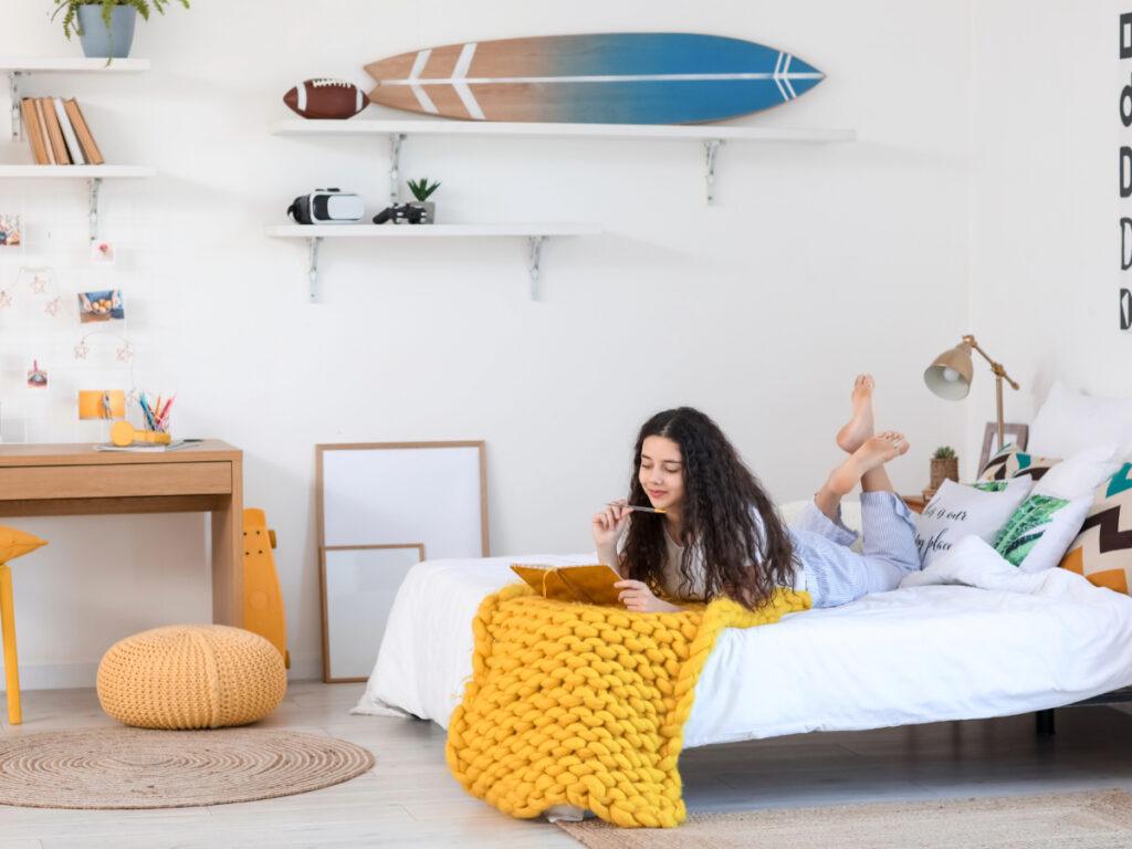 Teen girl laying on bed on laptop in thoughtfully designed bedroom