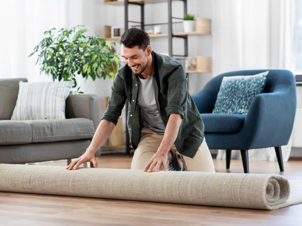 Smiling man unrolling a new rug in his rental apartment