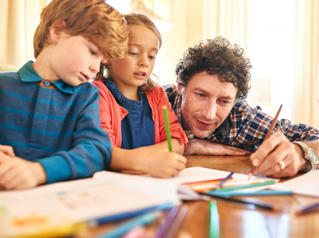 Father helping his two children with schoolwork at breakfast table